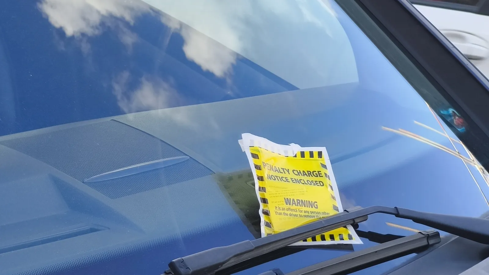 A yellow penalty charge notice envelope under a car's windscreen wiper